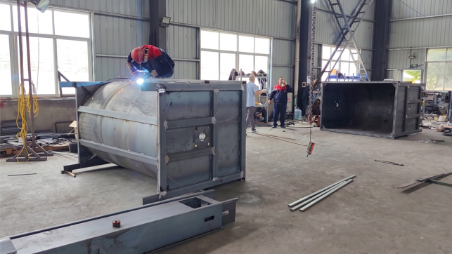 Skilled Xinhai worker in a red helmet actively welding a large steel drum structure in a modernized factory workshop